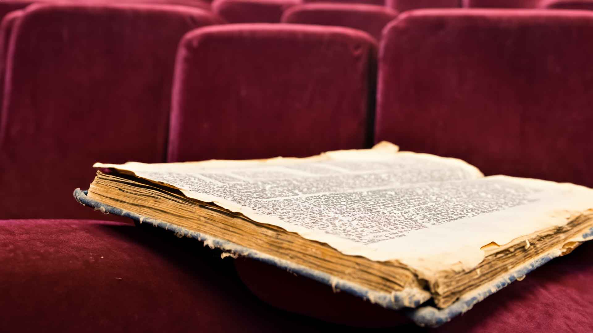 En gammal, trasig och dammig bok ligger uppslagen på ett säte i en teatersalong.