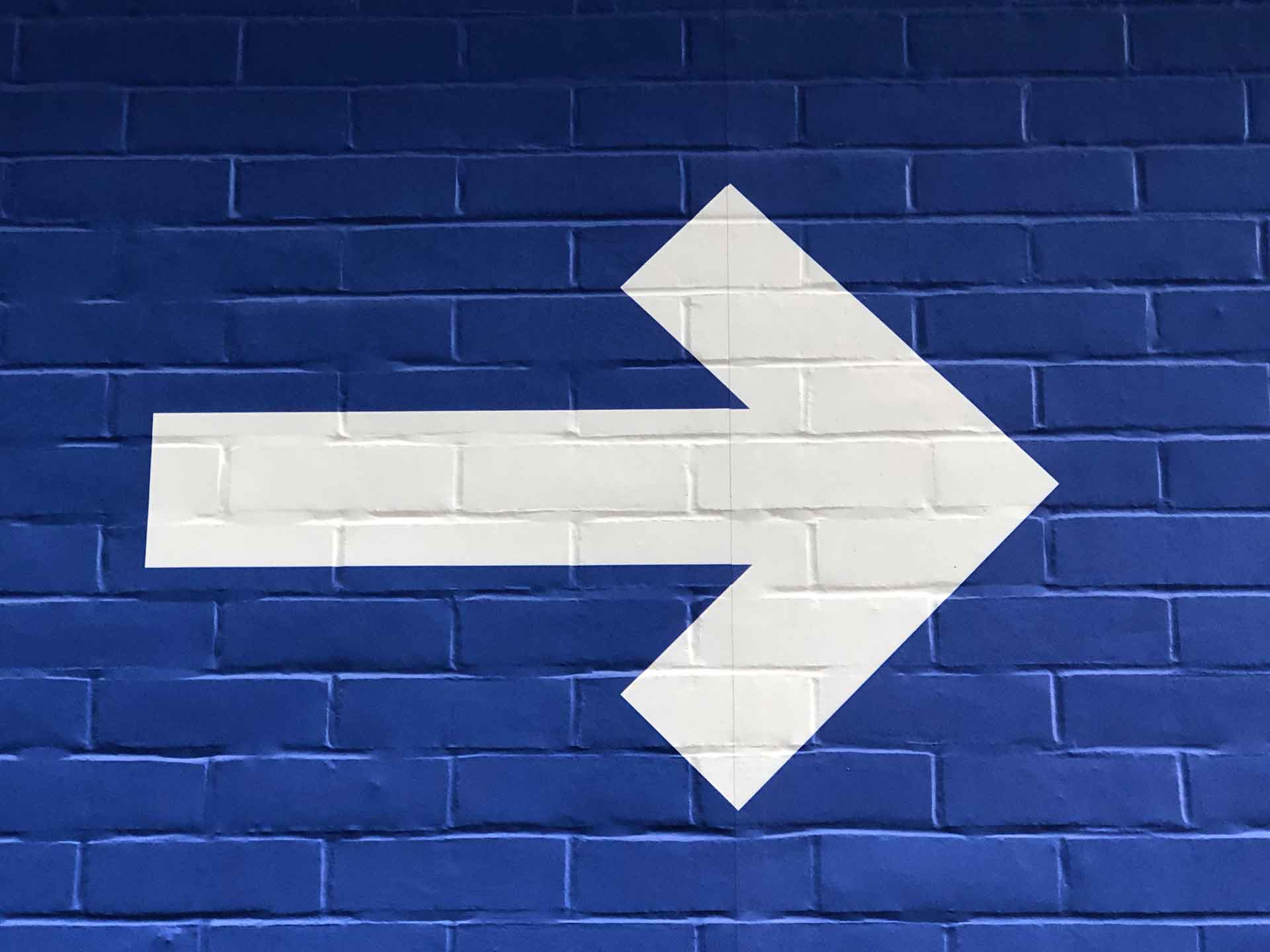 Vit högerpil målad på en blå tegelvägg.